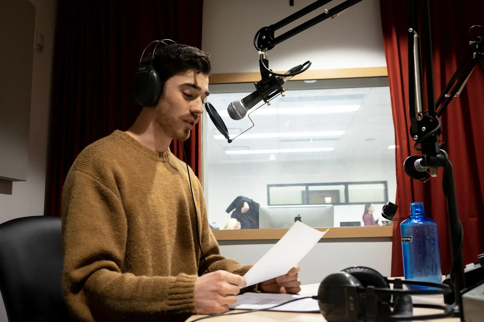 Michael A. Smith in a radio studio, wearing headphones and reading a script into a microphone