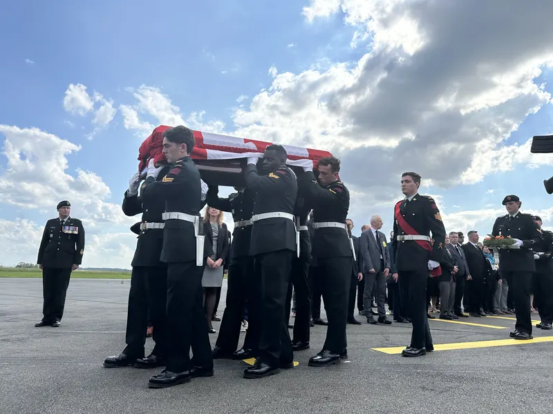Pallbearers in uniform carry a flag-draped casket across an airport tarmac